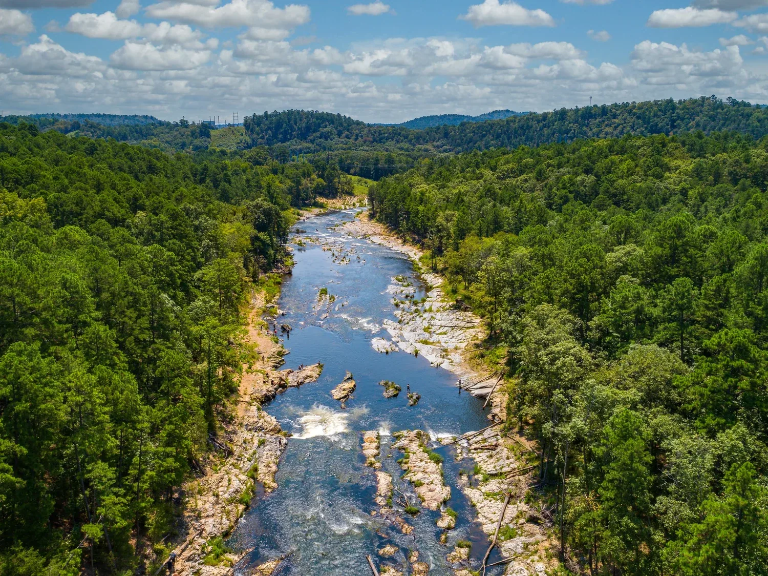 Aerial view of the Lower Mountain Fork River flowing through pine forest below the Broken Bow dam