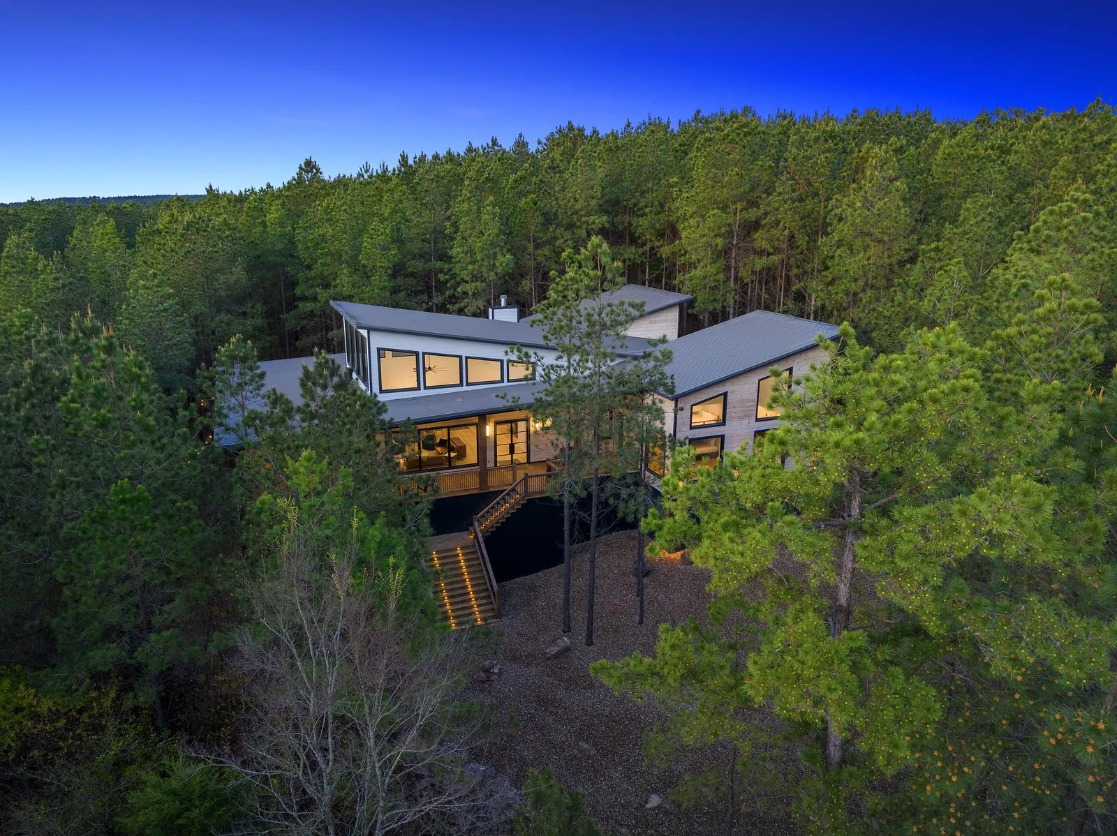 Aerial view of The Arcadia modern luxury cabin among pine trees at dusk in Hochatown