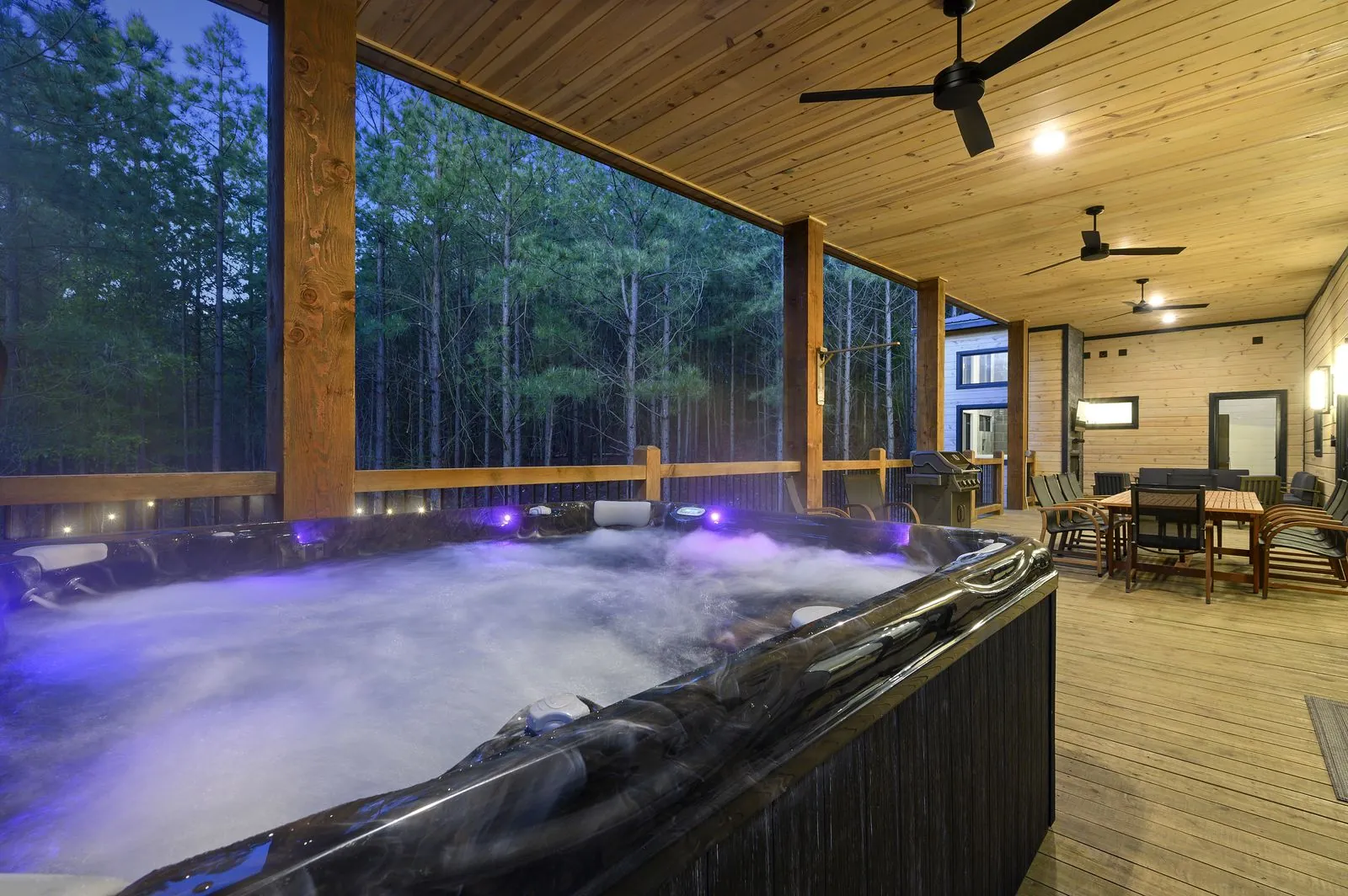Hot tub with purple LED lighting on the covered deck at The Arcadia surrounded by forest at dusk