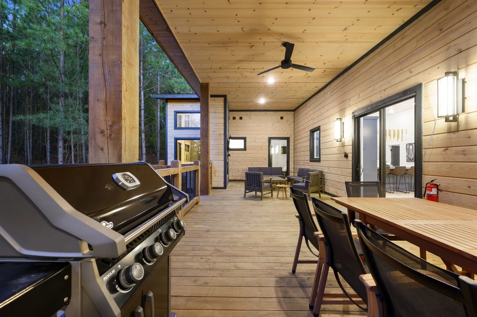 Covered deck at The Arcadia with ceiling fan, outdoor sectional, and interior chandelier visible through windows