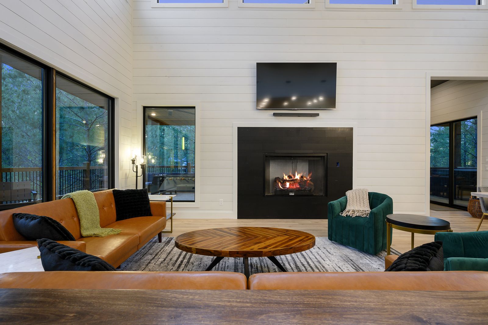 Living room at The Arcadia with camel leather sofas, emerald green chairs, linear fireplace, and shiplap walls