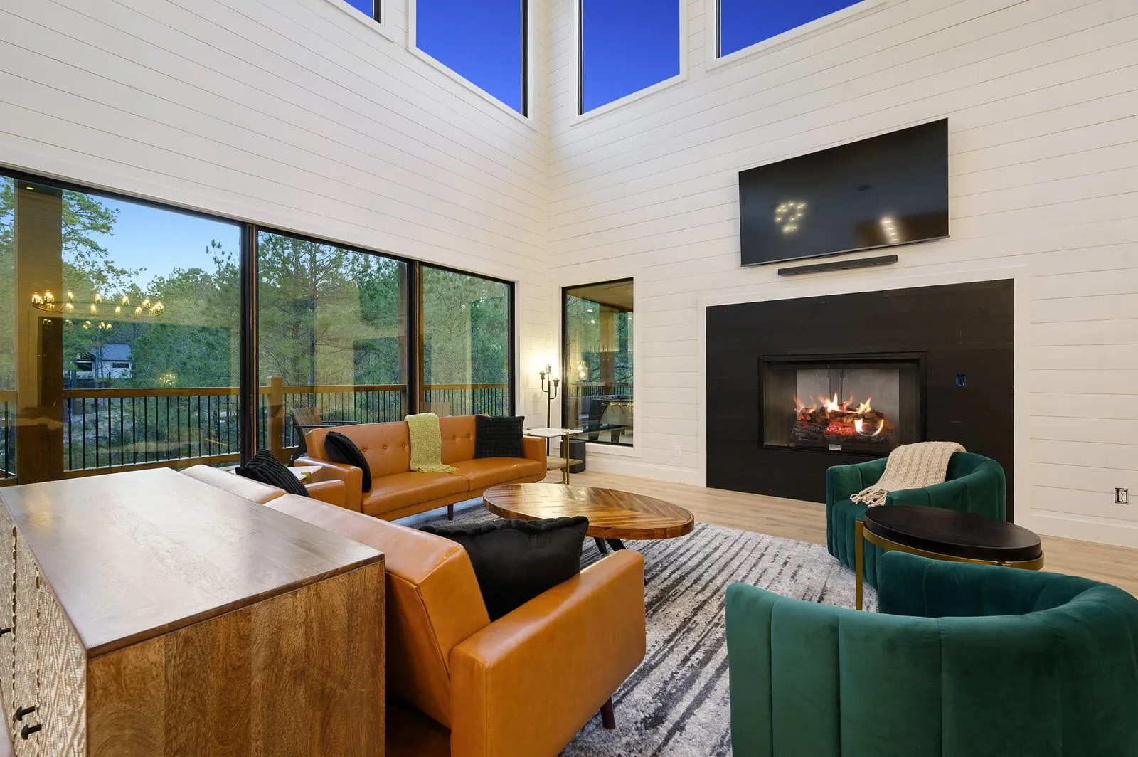 Covered deck exterior of The Arcadia showing living room through glass walls with string lights at dusk