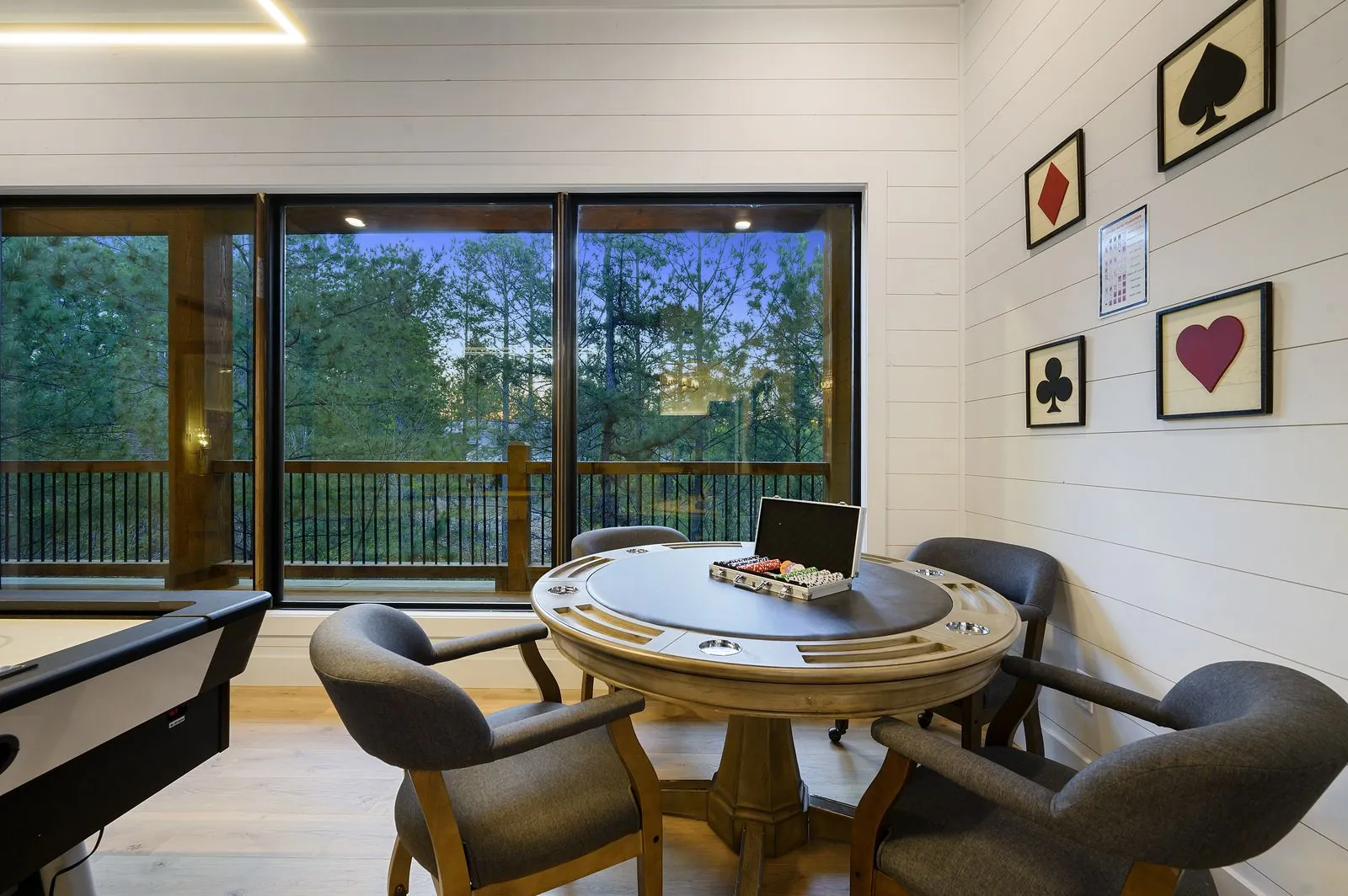 Poker table with gray upholstered chairs and playing card suit wall art on covered porch at The Arcadia