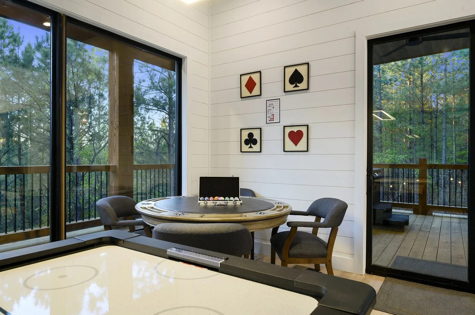 Poker room at The Arcadia with round table, card suit artwork, and views into the forest