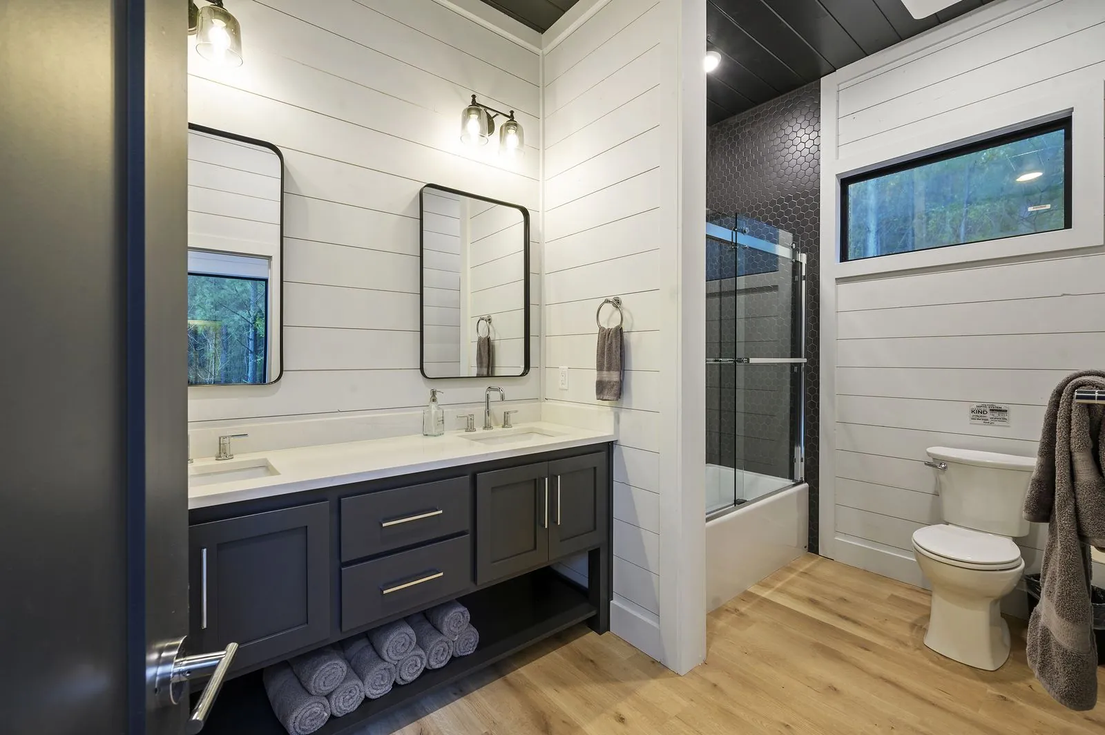 Bathroom at The Arcadia with navy double vanity, dual black-framed mirrors, and shiplap walls