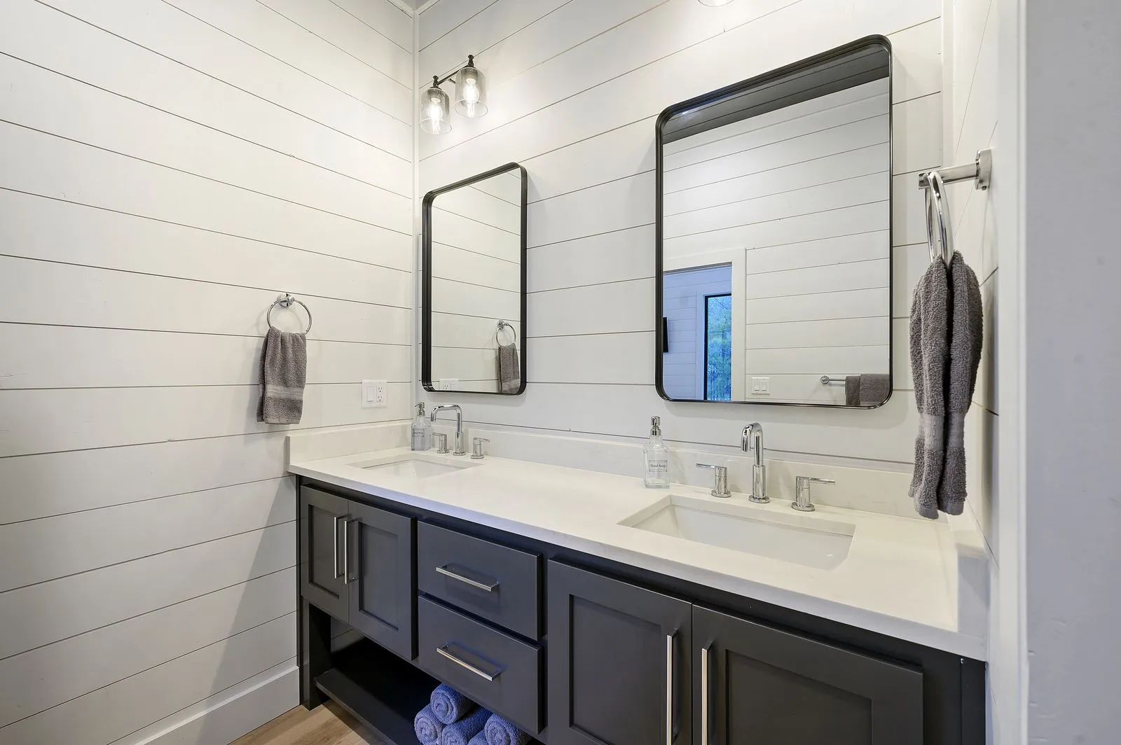 Double vanity bathroom at The Arcadia with navy blue cabinets, brass hardware, and white countertops