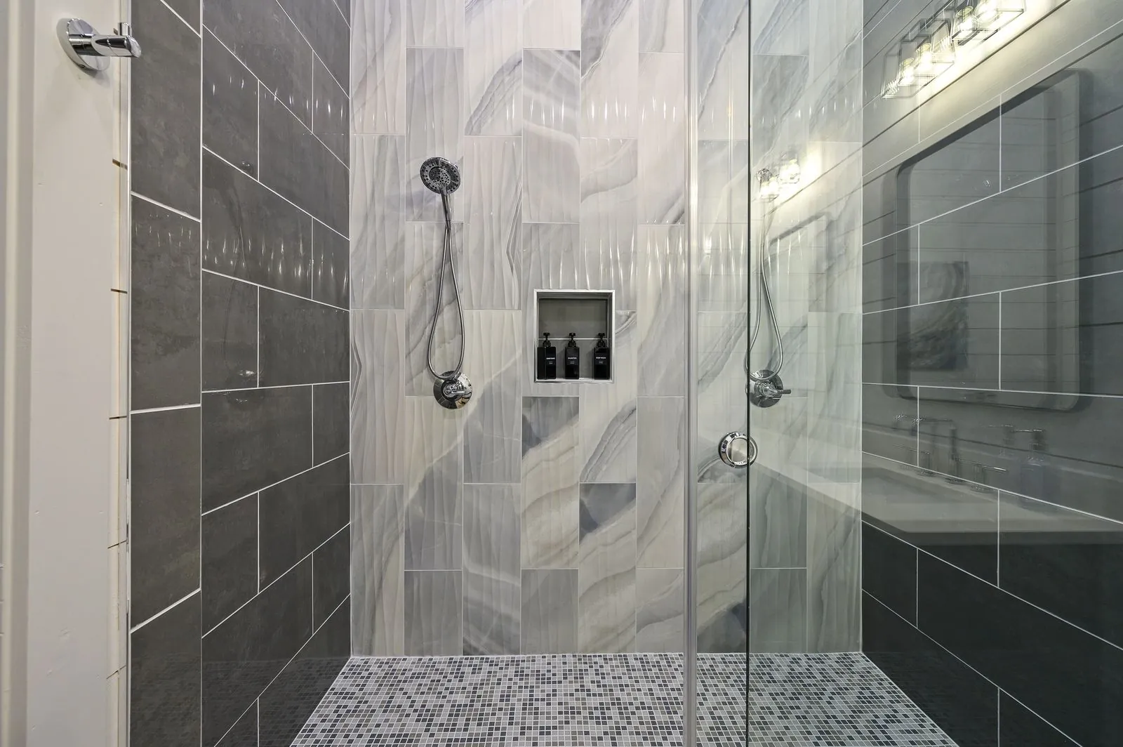 Walk-in shower at The Arcadia with dual showerheads, dark marble tile, and built-in toiletry niche