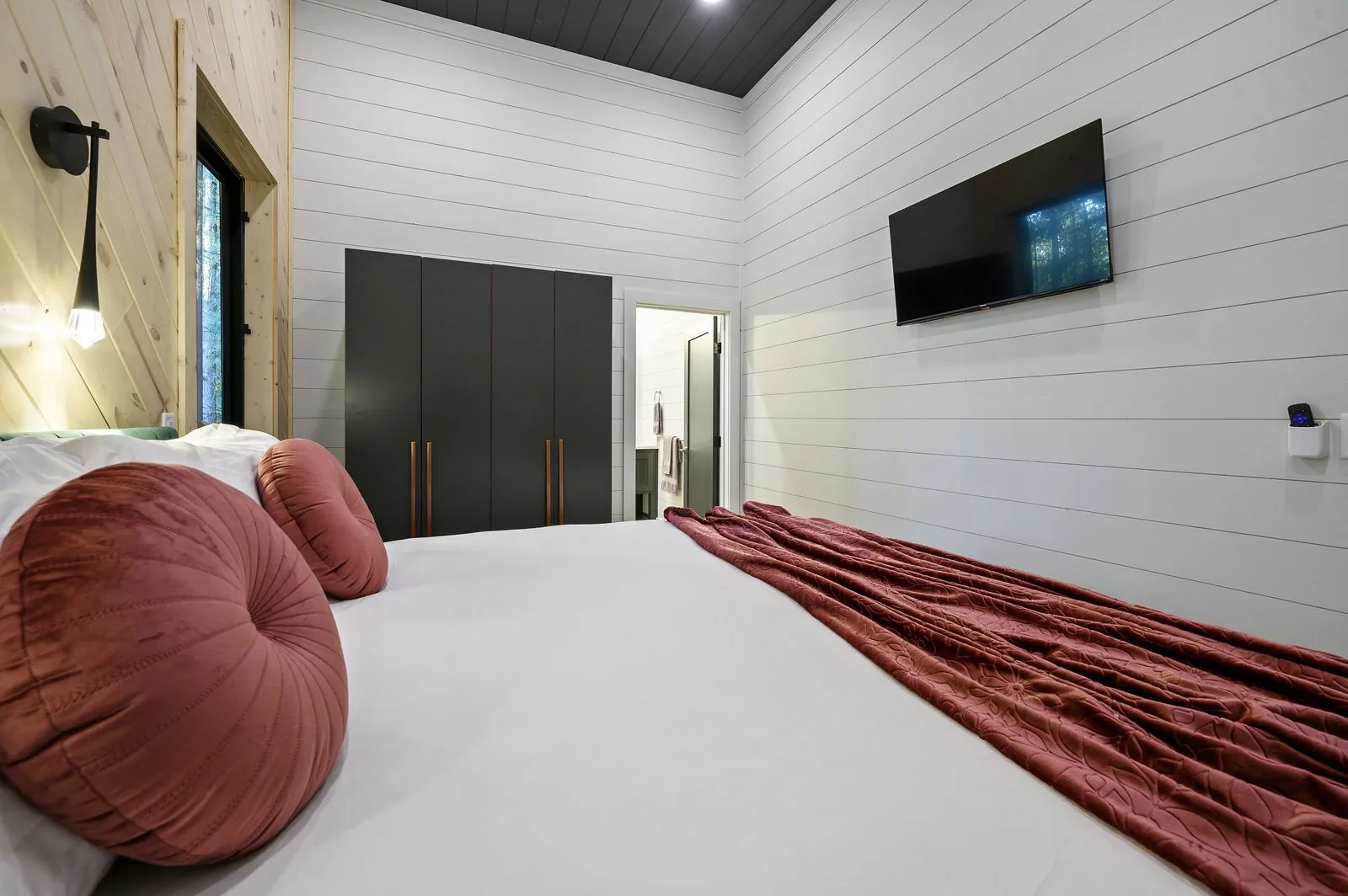 King bedroom at The Arcadia with dark green accent wall, red velvet throw, and ensuite bathroom entry