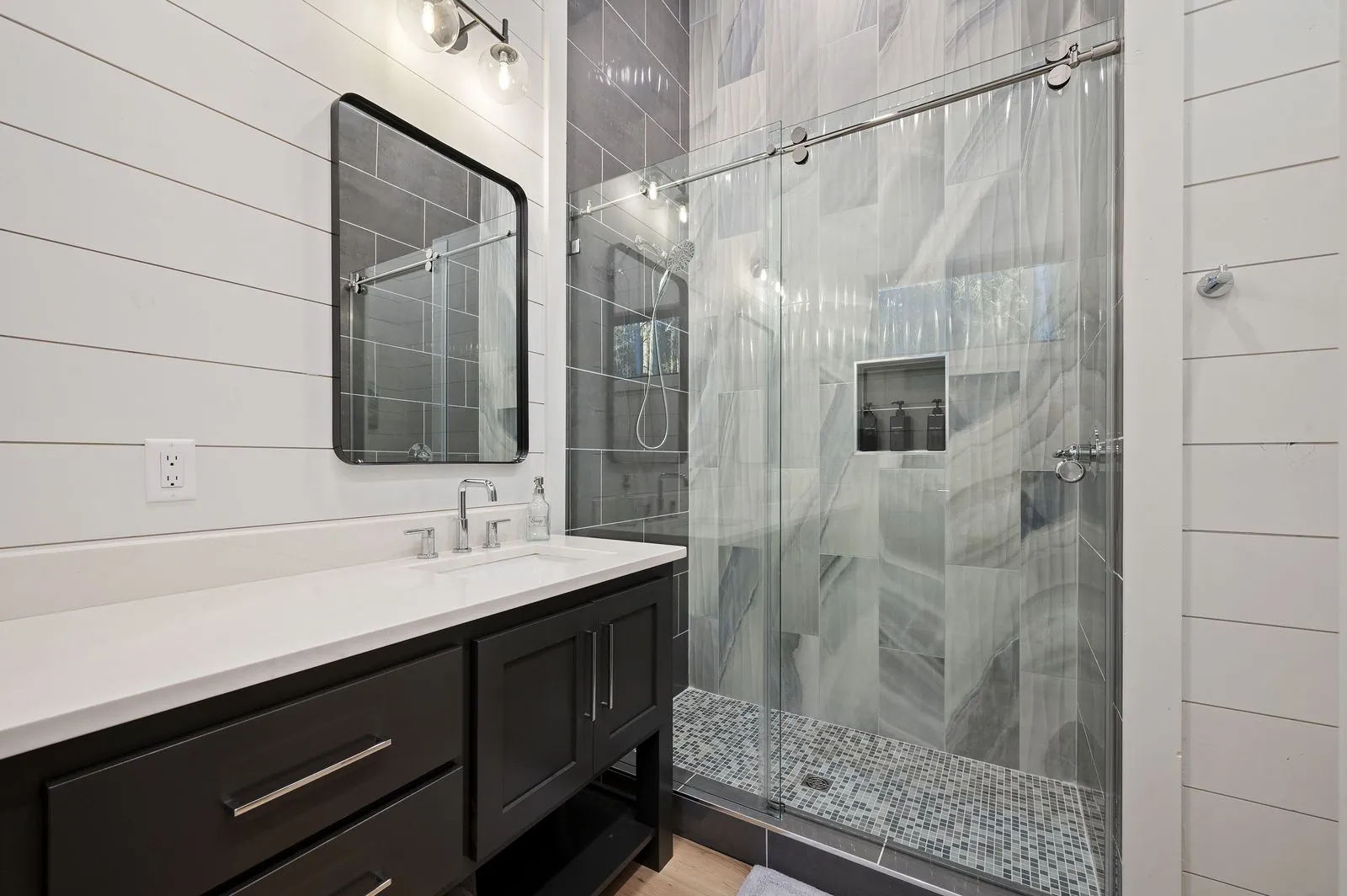 Bathroom vanity at The Arcadia with dark cabinets, dual undermount sinks, and large framed mirror