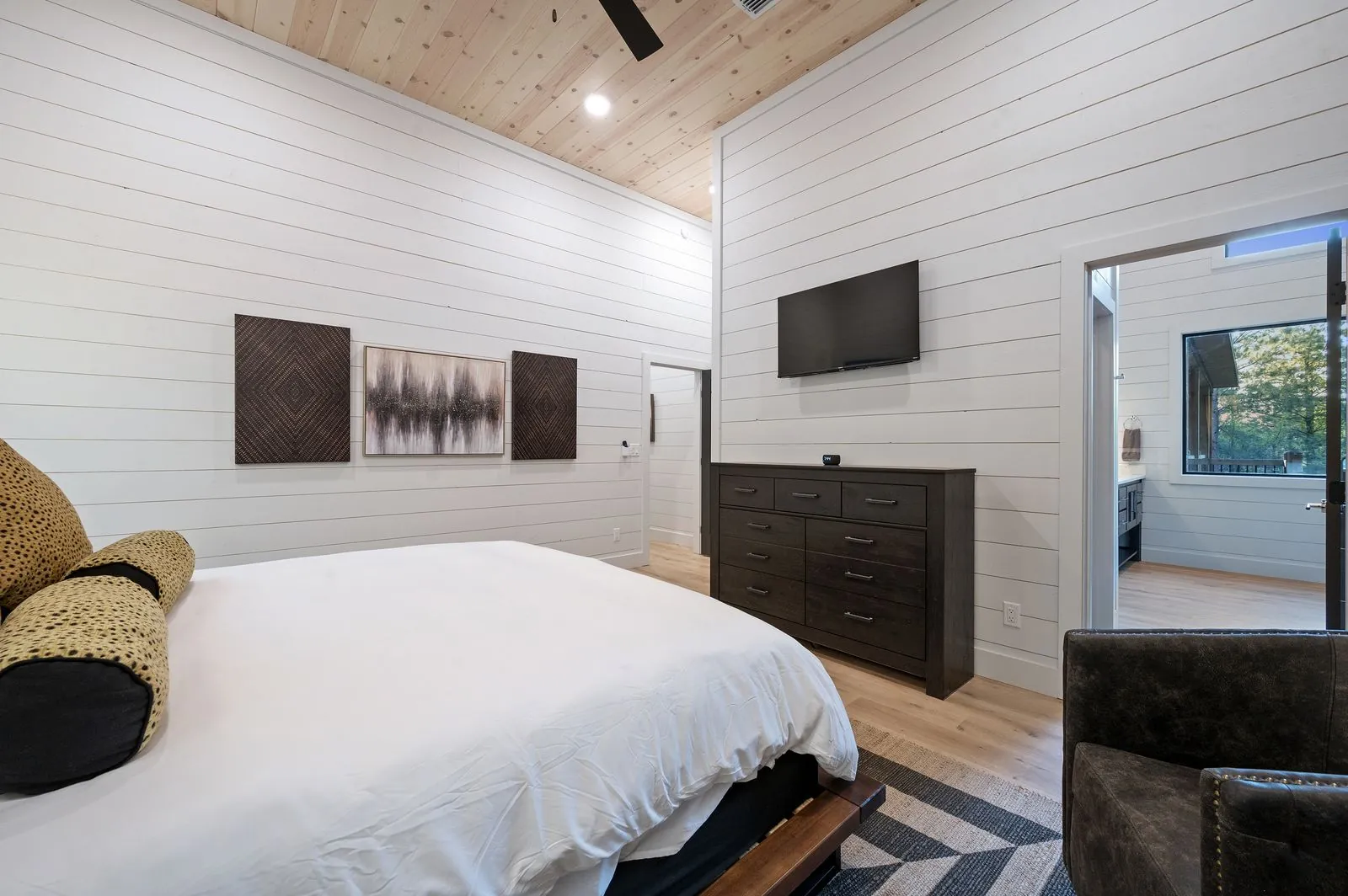 King bedroom at The Arcadia with navy blue throw, dark dresser, and floor-to-ceiling forest-view windows