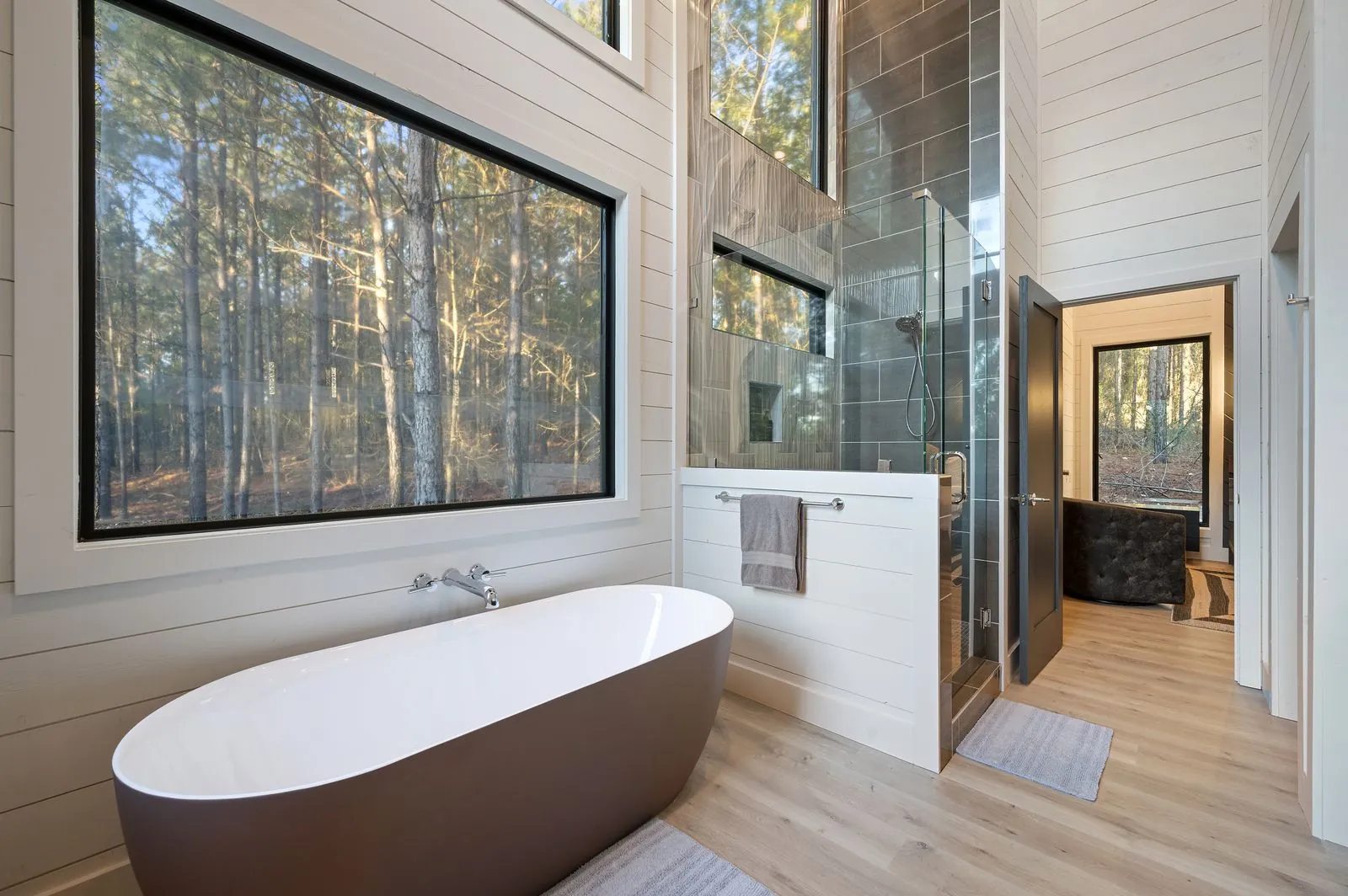 Primary bathroom at The Arcadia showing freestanding tub and walk-in shower with forest views through glass