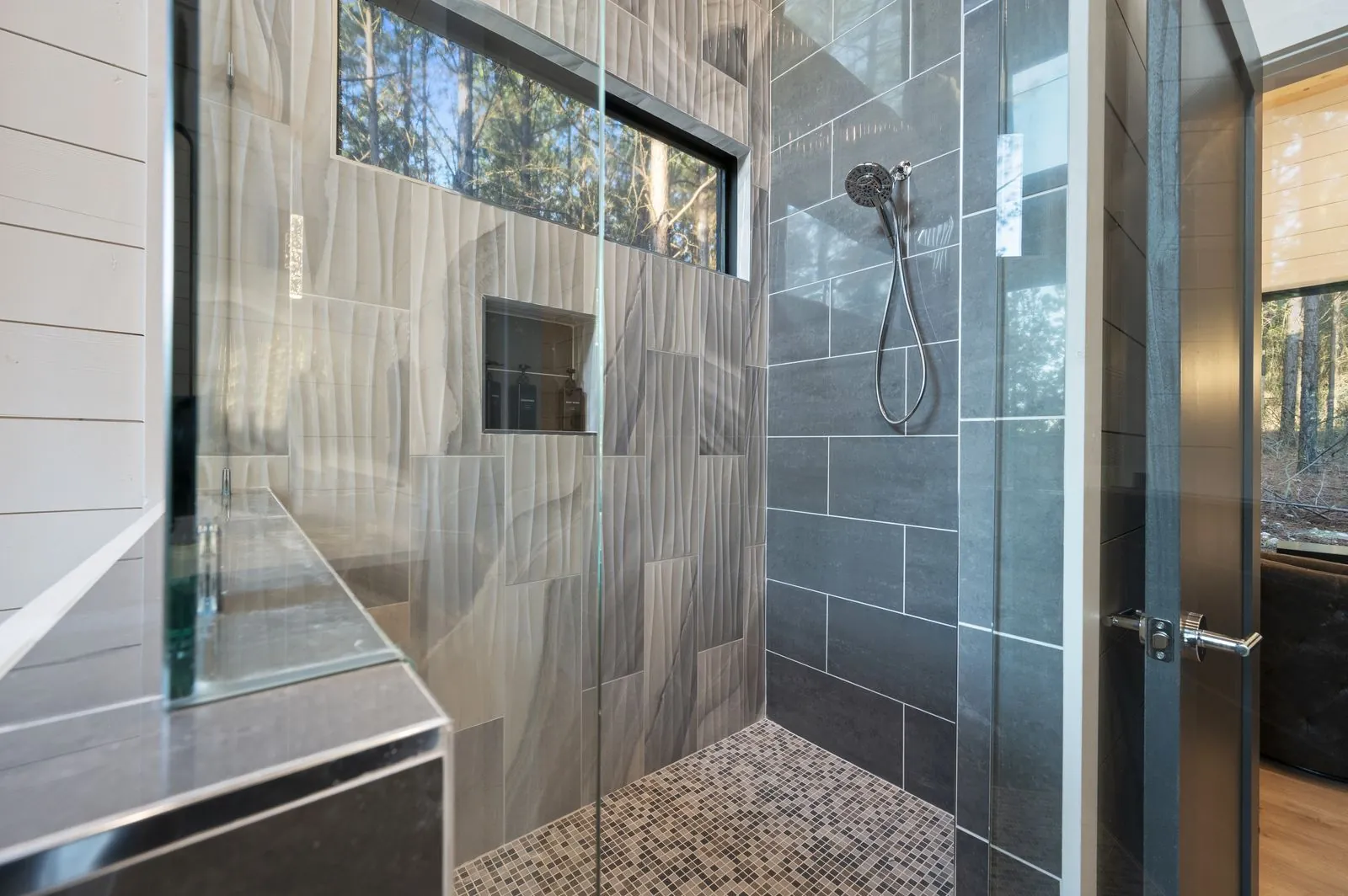Walk-in shower at The Arcadia primary bathroom with marble swirl tile and forest-view window