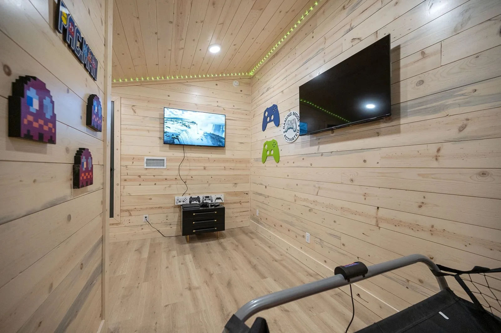 Gaming corner at The Arcadia lower level with large TV, game controllers, and green LED accent lighting