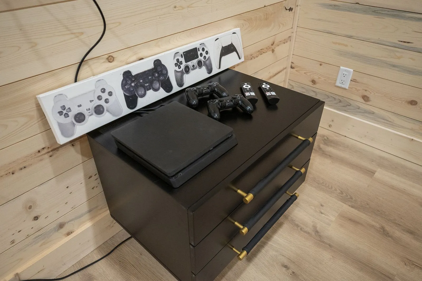 Gaming console station at The Arcadia with controllers displayed on black dresser and wood-paneled walls
