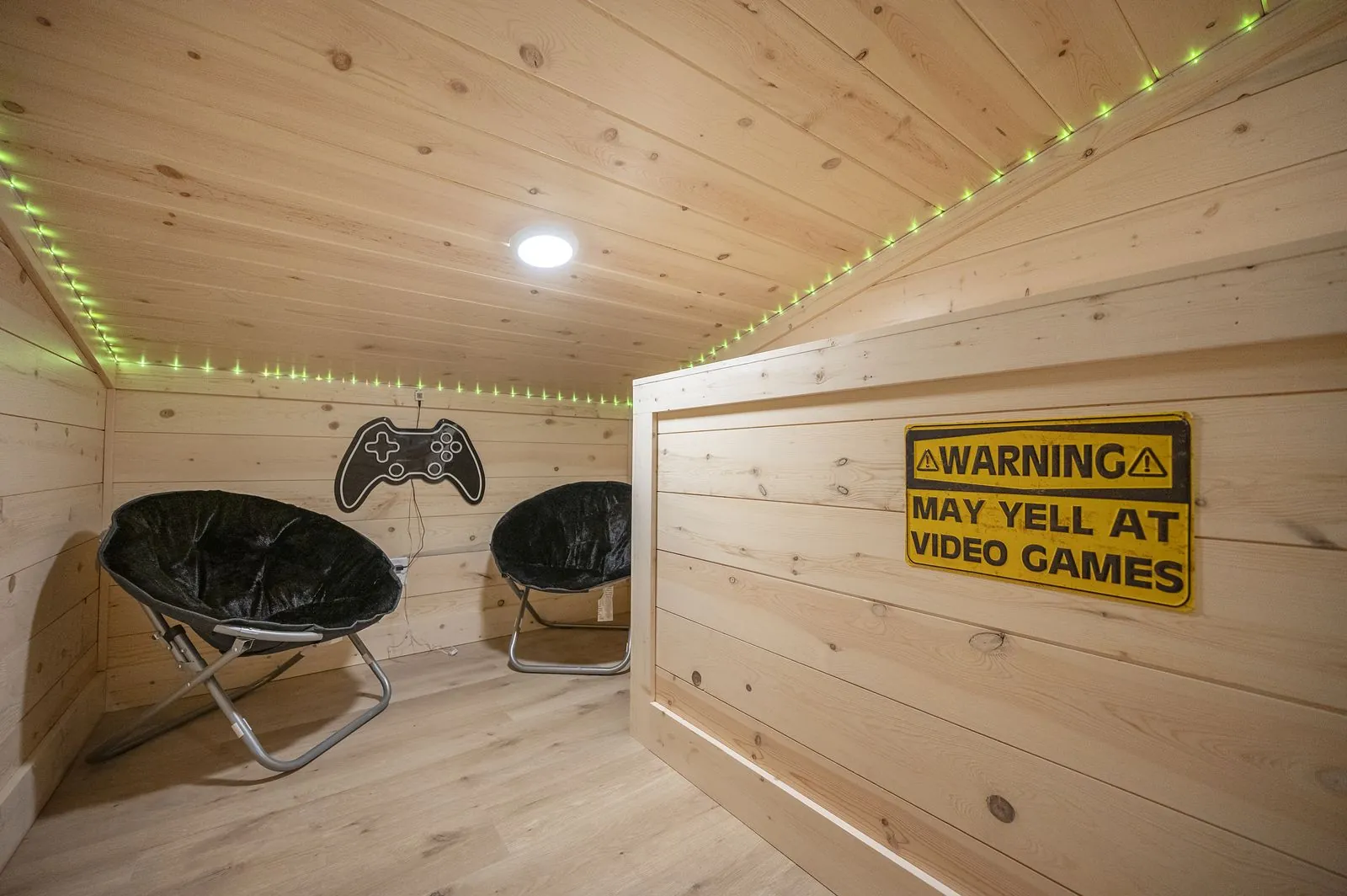 Gaming nook at The Arcadia with wall-mounted TV, controller decals, and green LED strip lighting