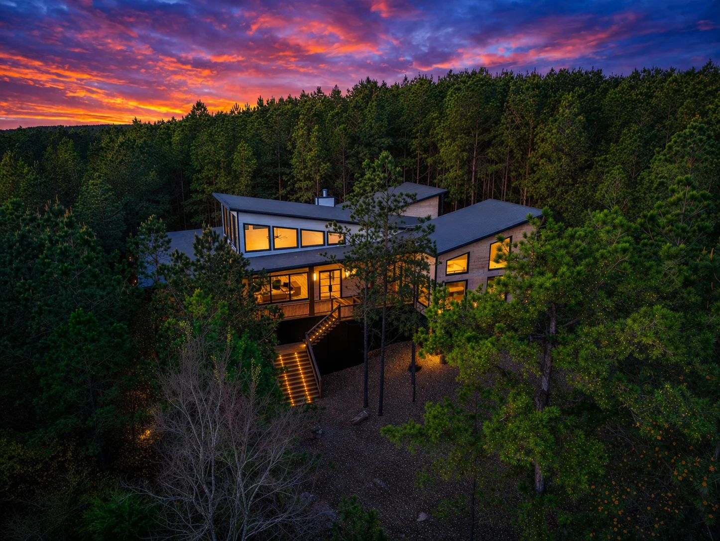 Aerial view of The Arcadia multi-level modern cabin among pine trees at dusk in Broken Bow