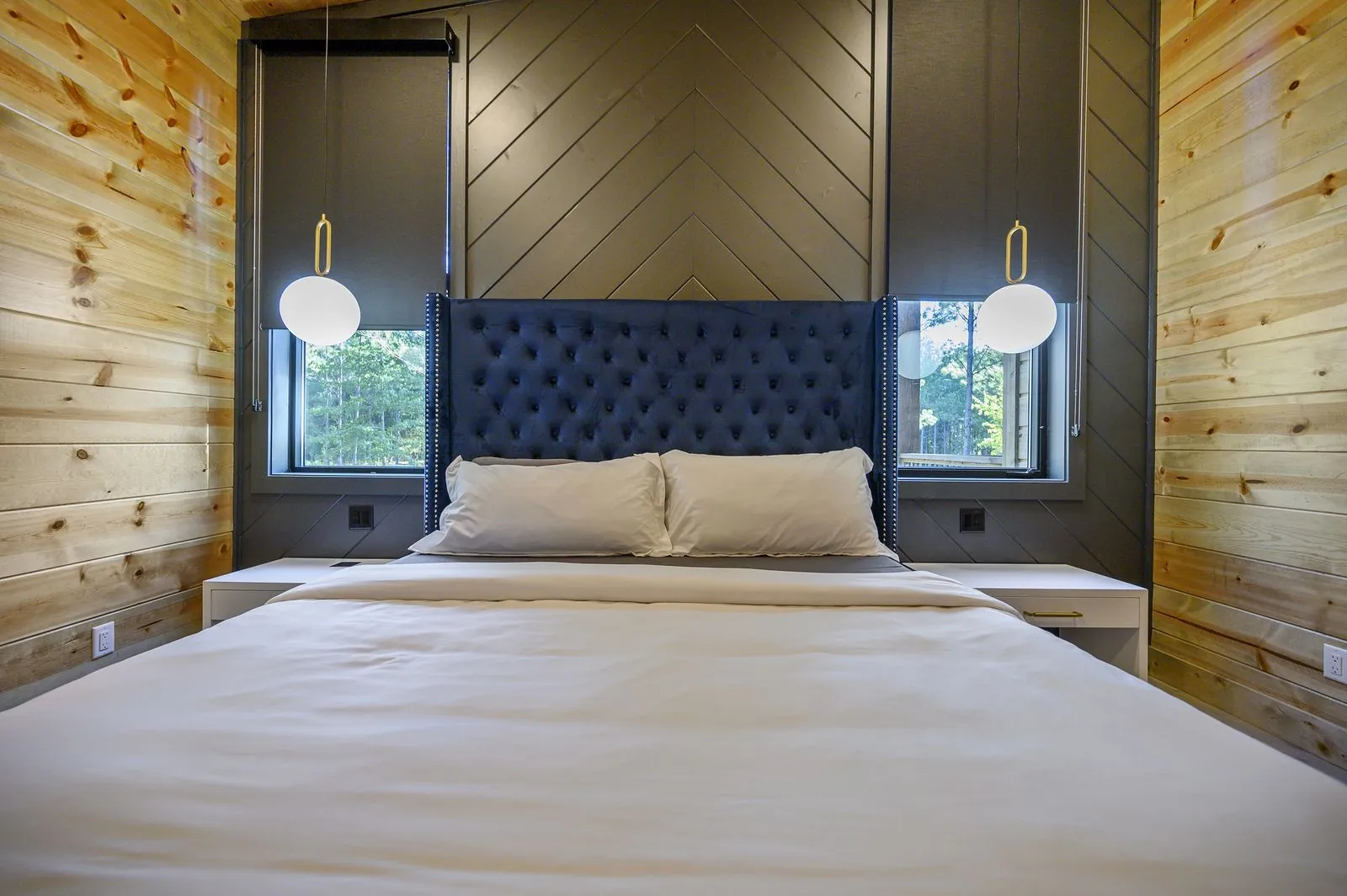 King bedroom at The Avalon with forest-view window, dark accent wall, and industrial sconce lighting