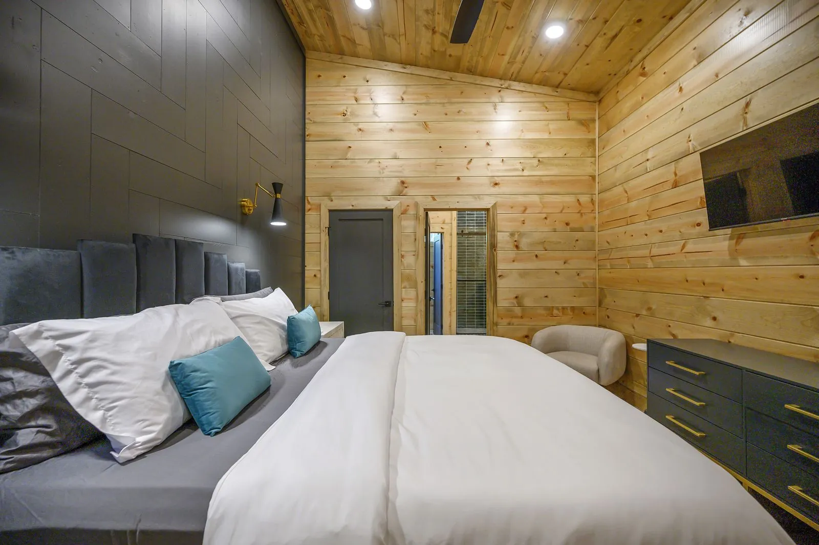 King bed at The Avalon with blue headboard, white bedding, and dark accent wall with TV