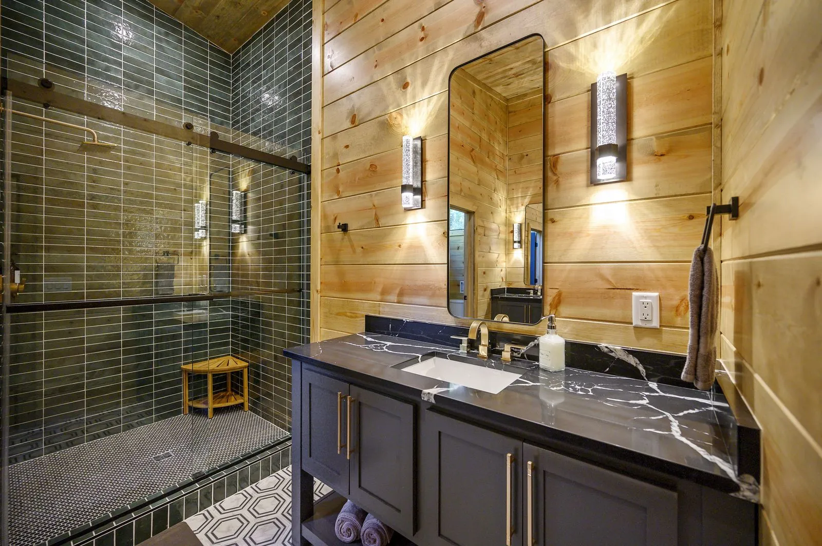Bathroom vanity at The Avalon with dark cabinet, black marble counter, rectangular mirror, and warm sconces