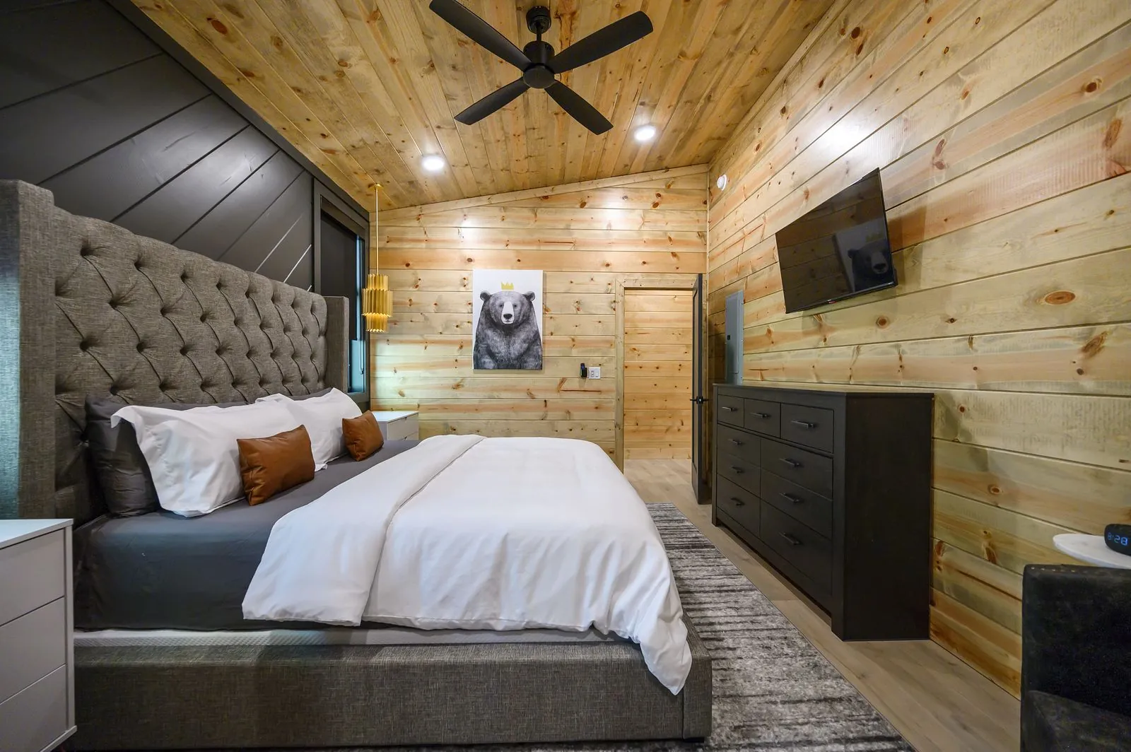 King bed at The Avalon with gray upholstered headboard, teal pillows, and dark gray accent wall