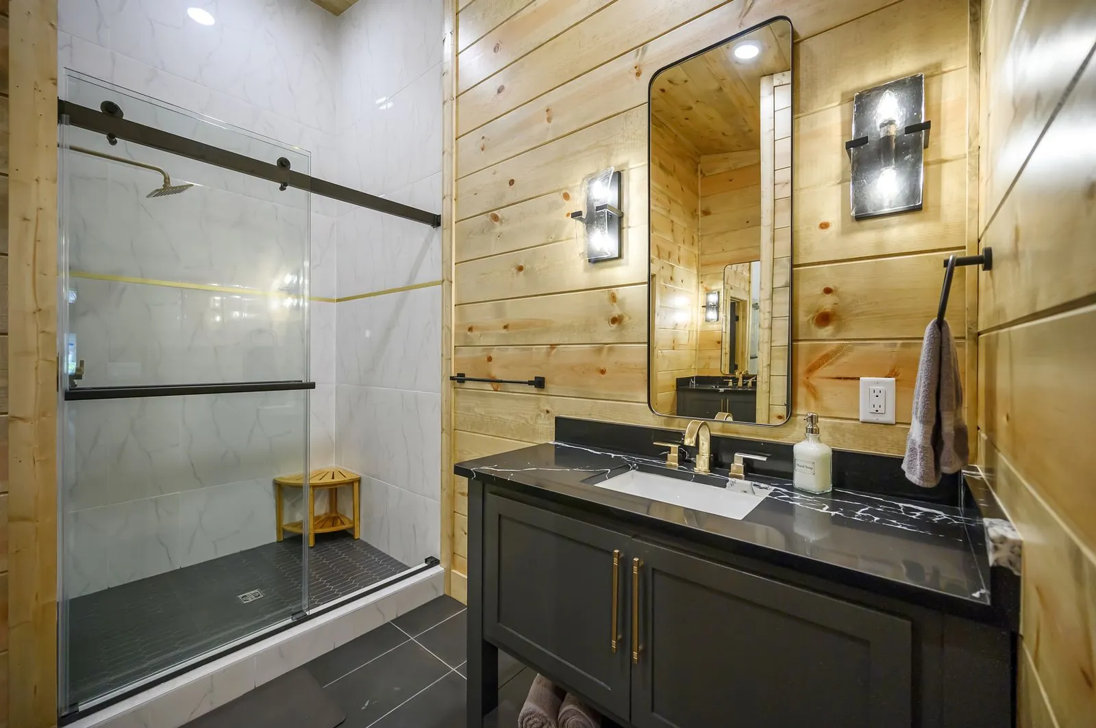 Walk-in shower at The Avalon with dark marble walls and gold rain showerhead on bamboo stool