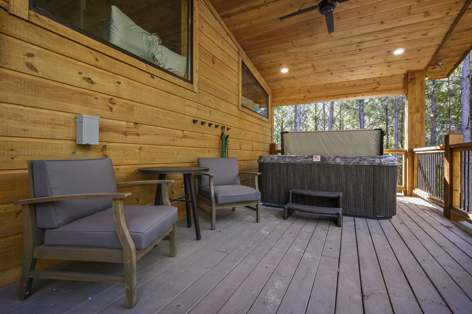 Covered deck with dining area and BBQ grill at The Avalon surrounded by tall pine trees