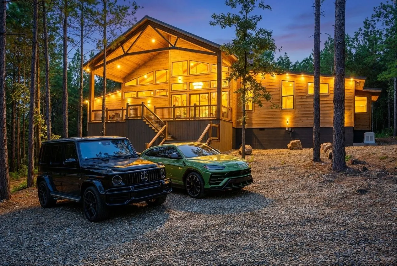 Front exterior of The Avalon at twilight with parked vehicles, wraparound deck, and illuminated A-frame entrance