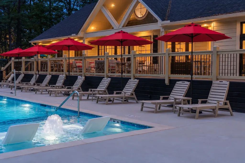 The Black-Beary — A shared resort pool with a water fountain feature, lined with lounge chairs and red umbrellas, included at no extra cost. The lodge building behind offers additional covered seating.