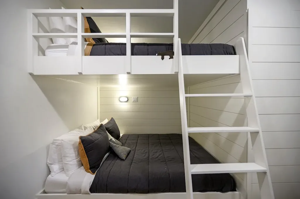 The Black-Beary — This bedroom has built-in queen-over-queen bunk beds with a fixed ladder, plus a window looking out onto trees.