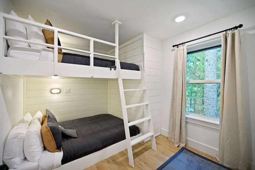 The Black-Beary — This bedroom has built-in queen-over-queen bunk beds with a fixed ladder, plus a window looking out onto trees.