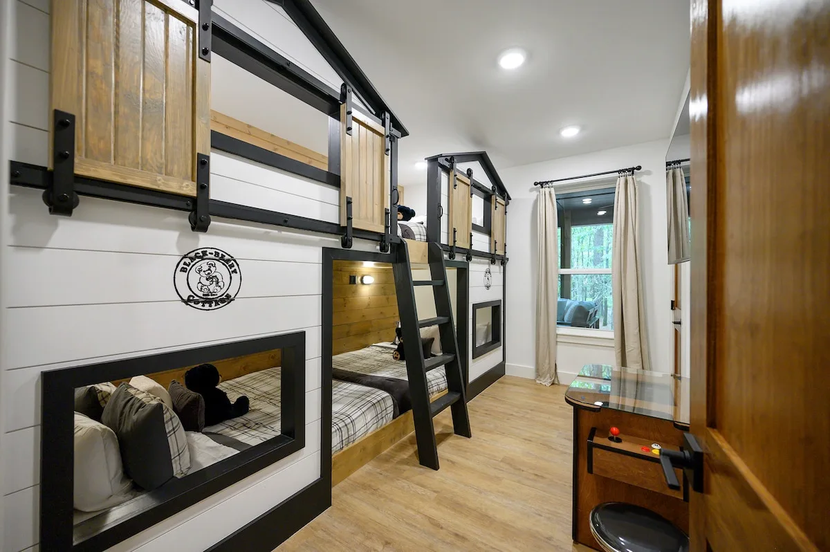 Bunk room with barn-door bed nooks and tabletop arcade game