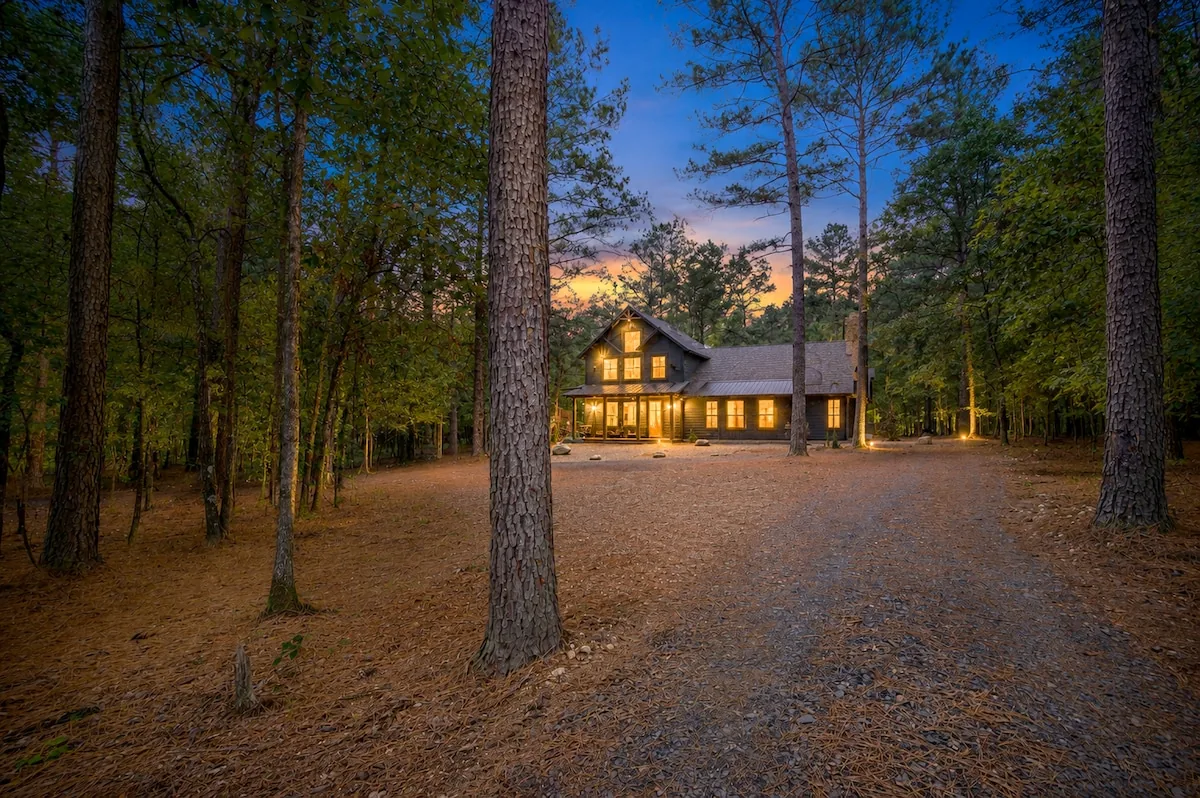The Black-Beary luxury cabin at twilight with glowing windows and a gravel drive through the pines