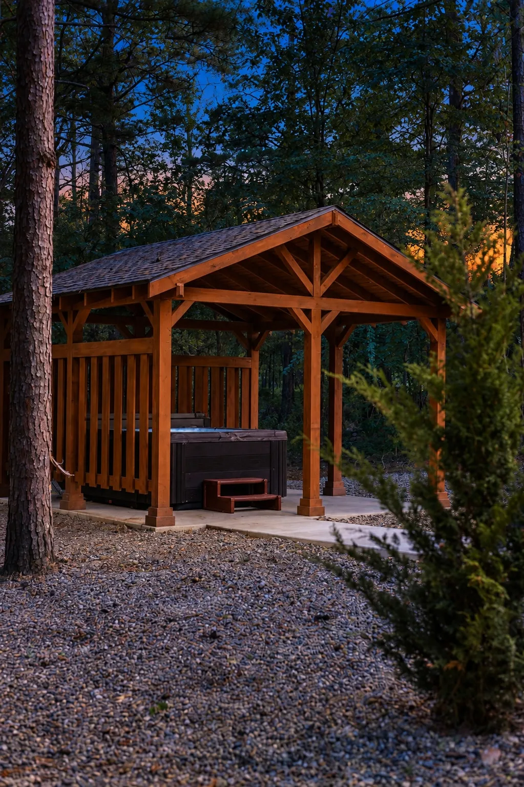 Dolce Far Nient — A covered wooden pavilion houses a private hot tub with steps for easy entry, set in the trees at dusk.