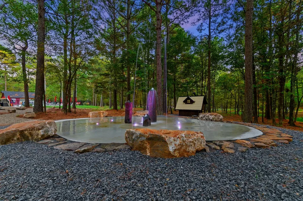 Dolce Far Nient — A shared splash pad with illuminated water jets sits among stone boulders in a wooded area of the resort, included at no extra cost.