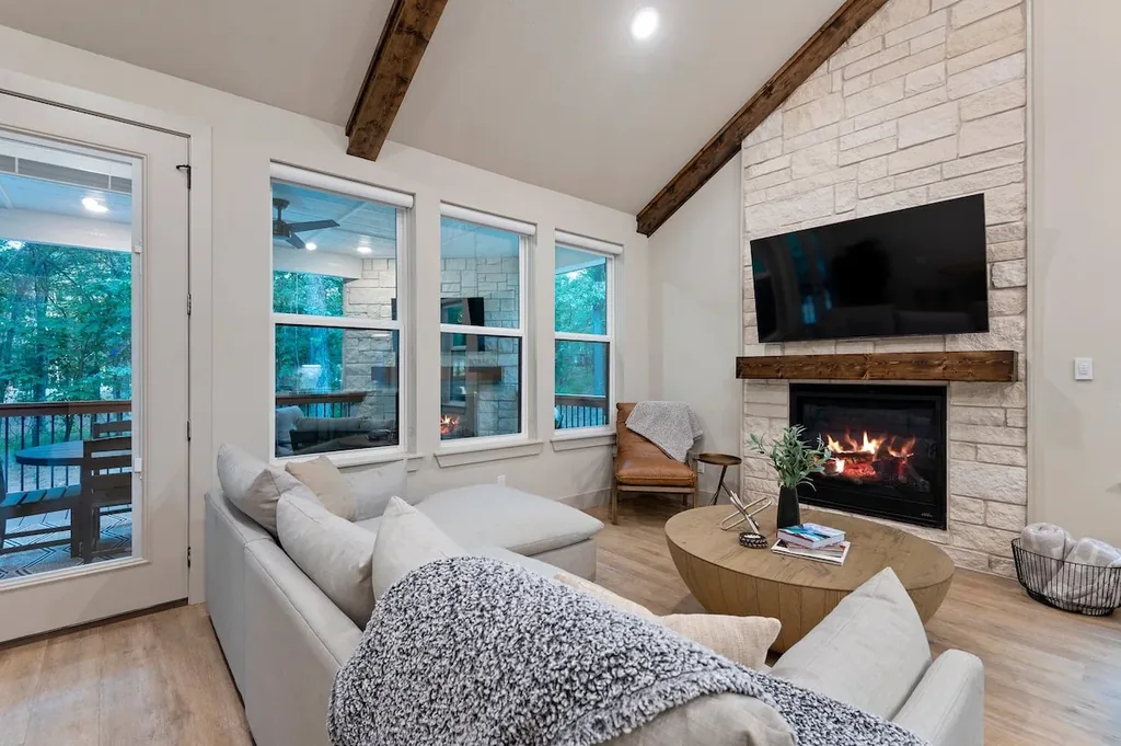 Dolce Far Nient — The living room has a sectional sofa, wall-mounted TV above a stone gas fireplace, and vaulted ceilings with exposed wood beams.