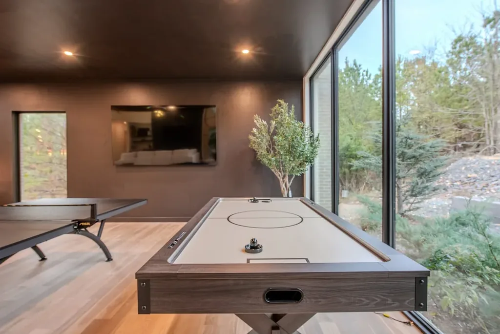 Air hockey table beside floor-to-ceiling forest views