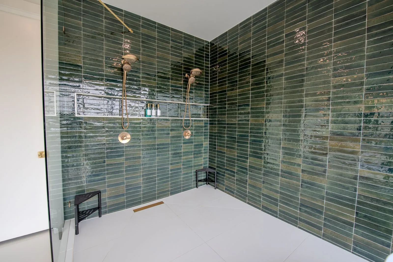 Spa bathroom entrance at The Jade featuring green tile walls, glass shower enclosure, arched mirror, and hardwood floor transition