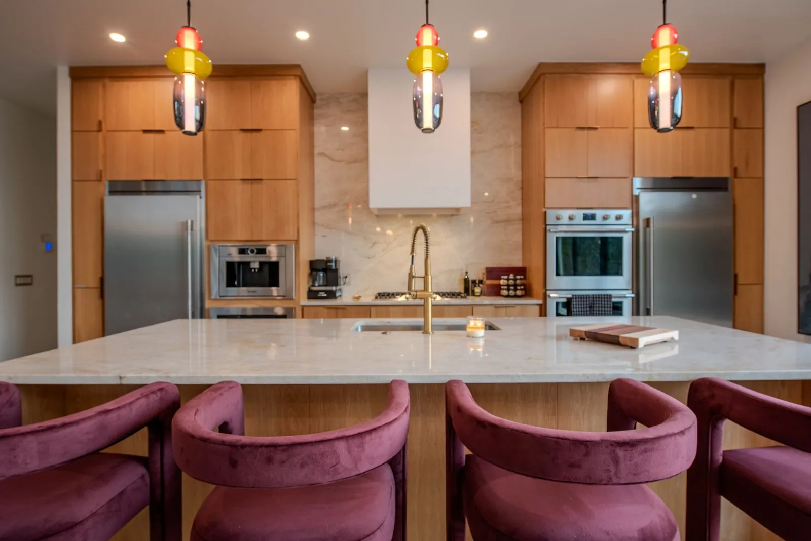 Kitchen detail at The Jade showing custom wood cabinetry, double wall ovens, marble countertops, and artisan pendant lighting