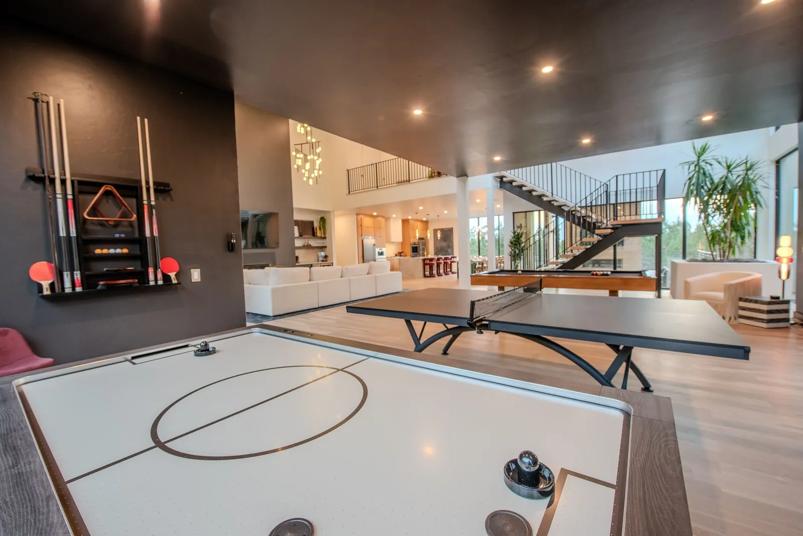 Lower-level game room at The Jade featuring air hockey table, ping pong, and dramatic spiral staircase with modern lighting