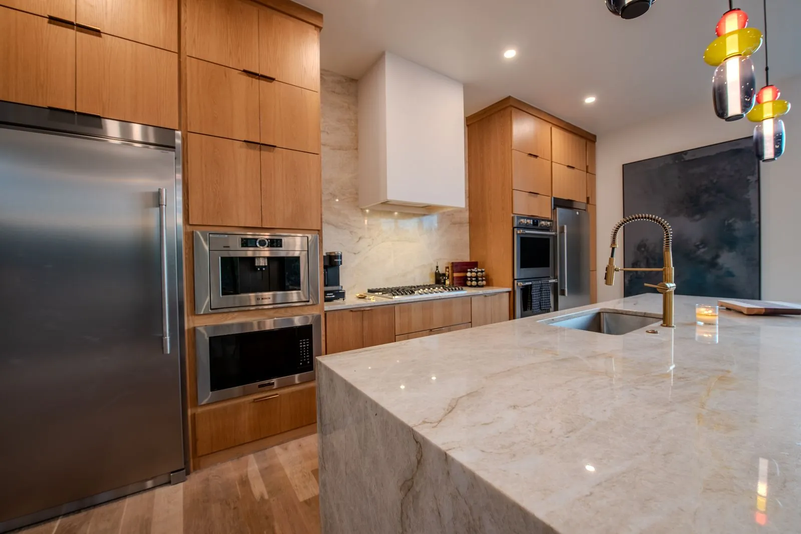 Kitchen view at The Jade featuring gold-accent pendant lights, stainless steel appliances, and marble countertop island