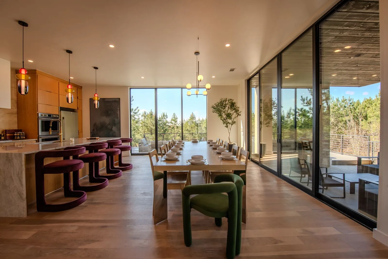 Dining area at The Jade with panoramic forest views through floor-to-ceiling glass walls and green upholstered accent chairs
