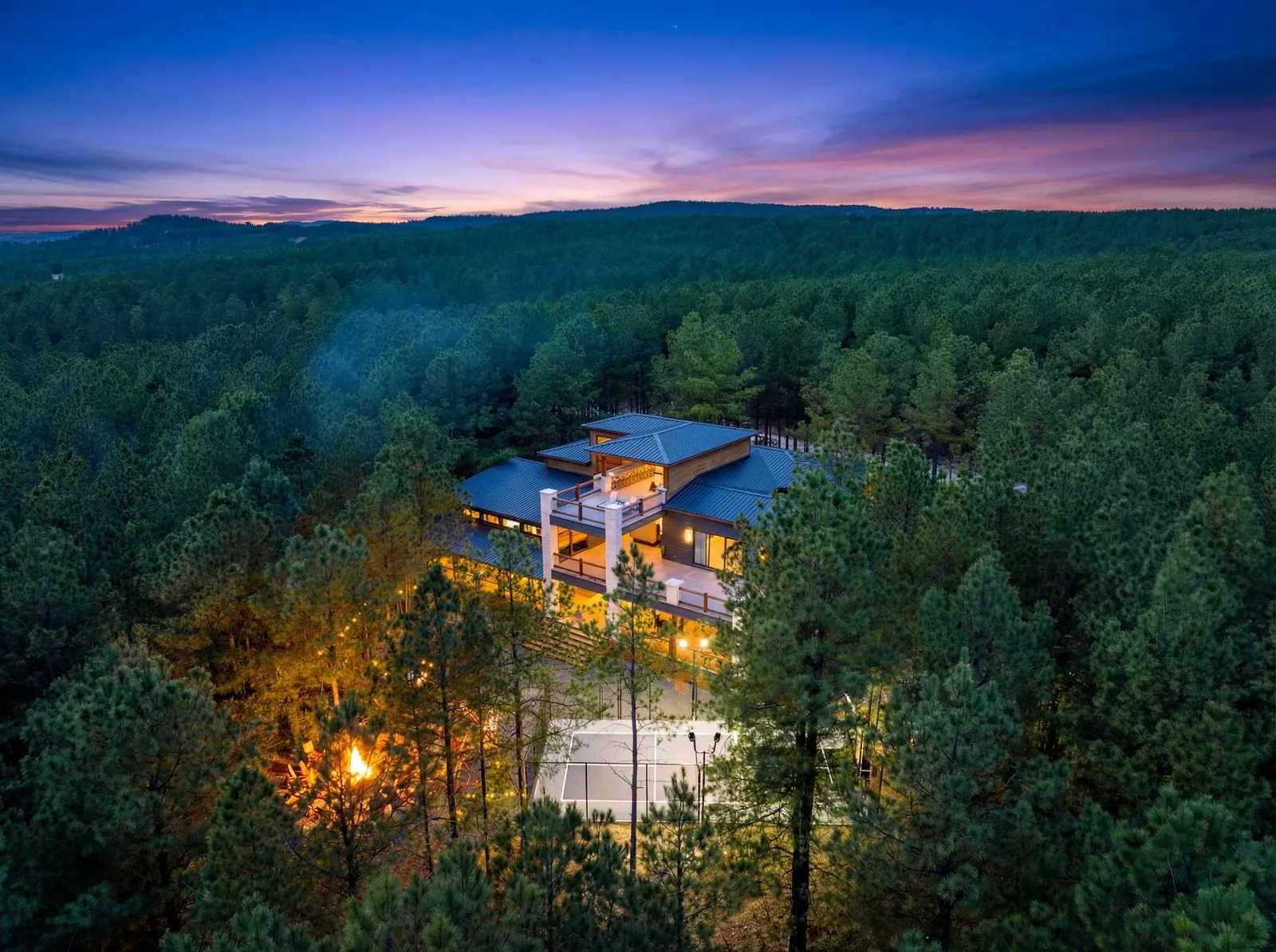 Aerial sunset panorama of LivNLove cabin showing full property with sport court, decks, and Broken Bow forest