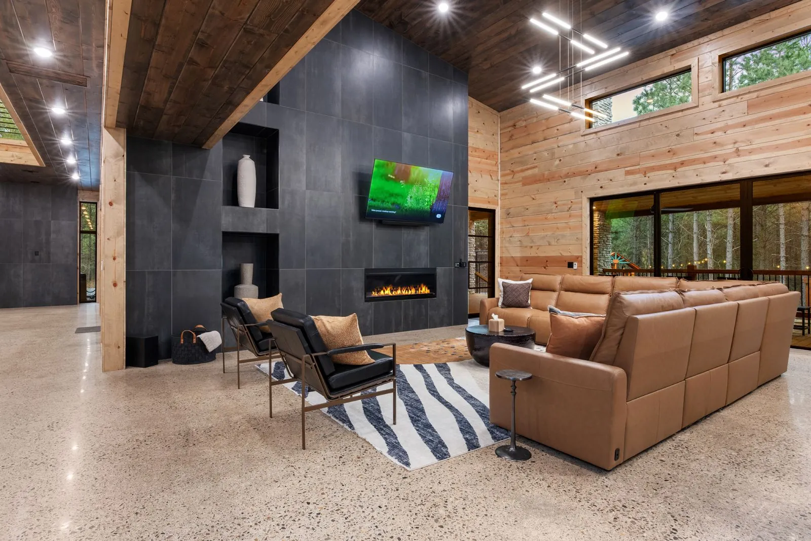 Double-height great room at LivNLove with vaulted wood ceiling, leather sectional, linear fireplace, and industrial staircase