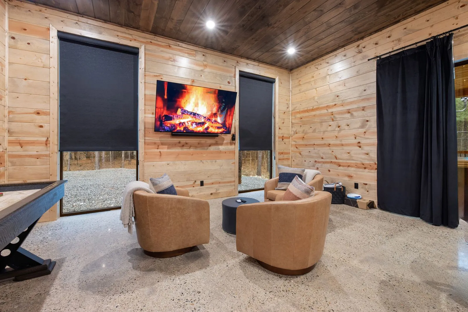 Conversation sitting area at LivNLove with leather armchairs, linear fireplace, and forest views through full-length curtains