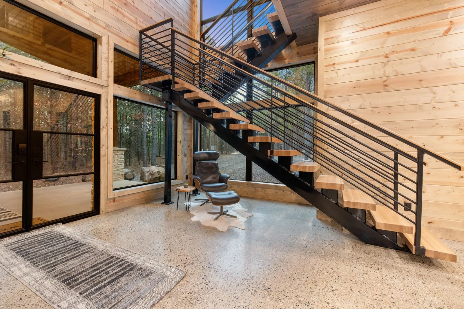 Open-concept main level at LivNLove showing industrial metal staircase, polished concrete floors, and tall windows