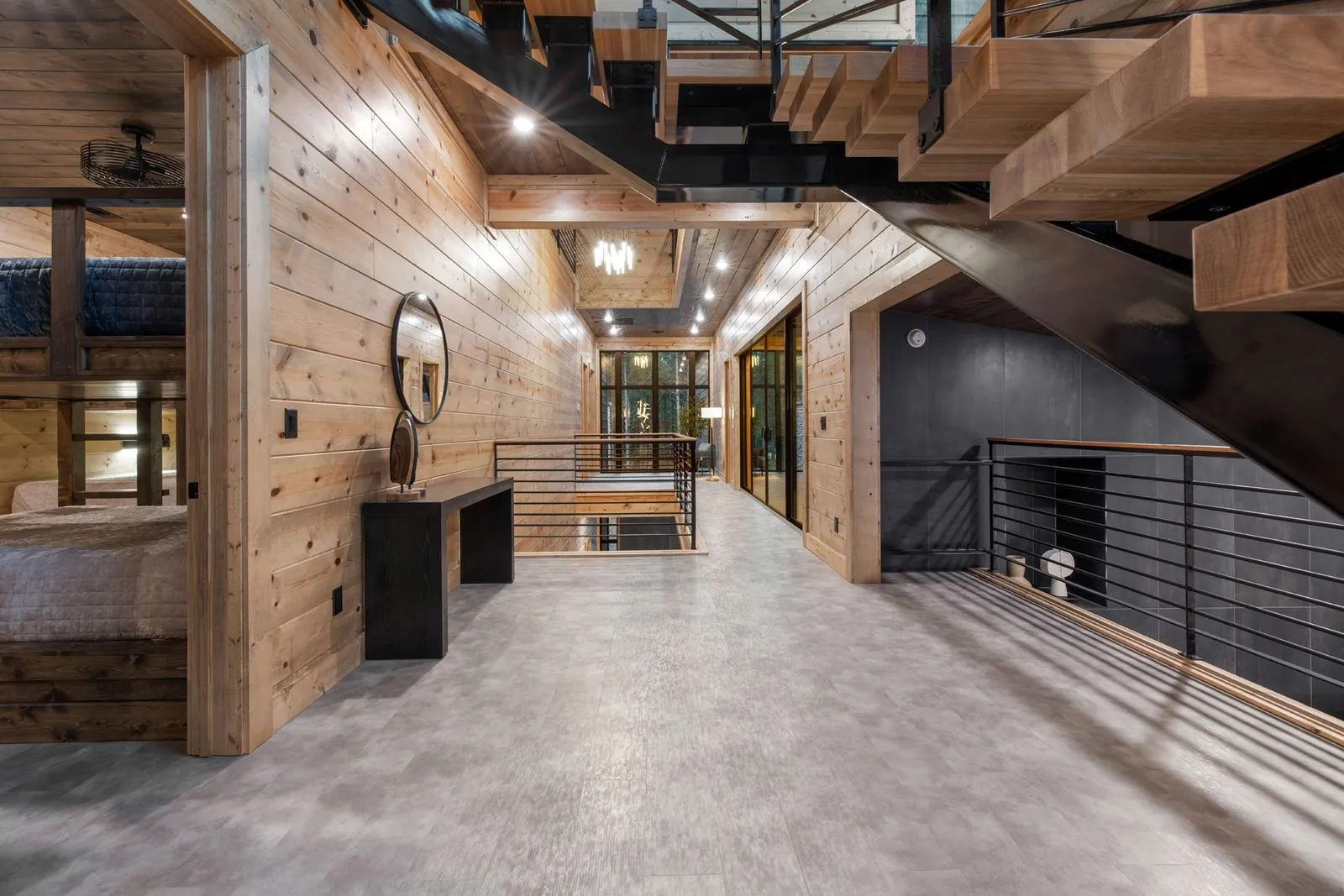 Upper loft hallway at LivNLove with metal railing, polished concrete floors, and warm wood walls