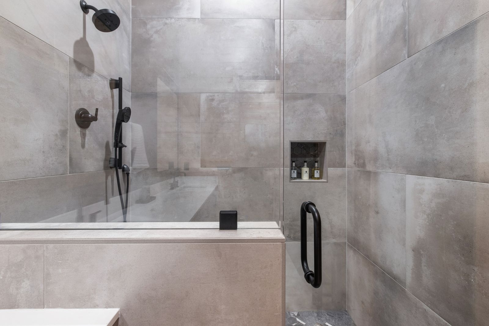 Walk-in shower with dark tile surround, rain showerhead, and frameless glass enclosure at LivNLove