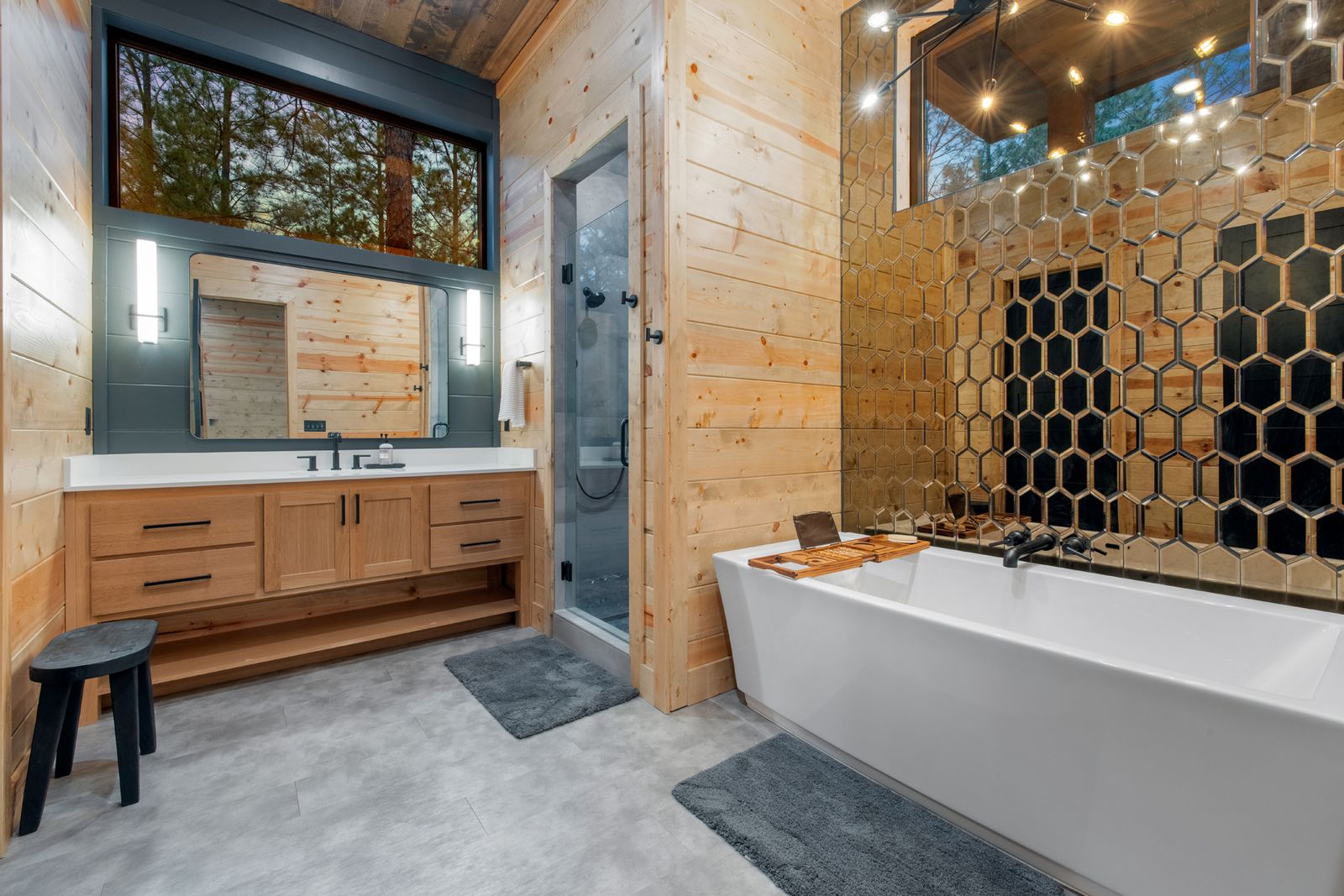 Freestanding bathtub with honeycomb hexagonal wall art, wood surround, and vanity mirror at LivNLove