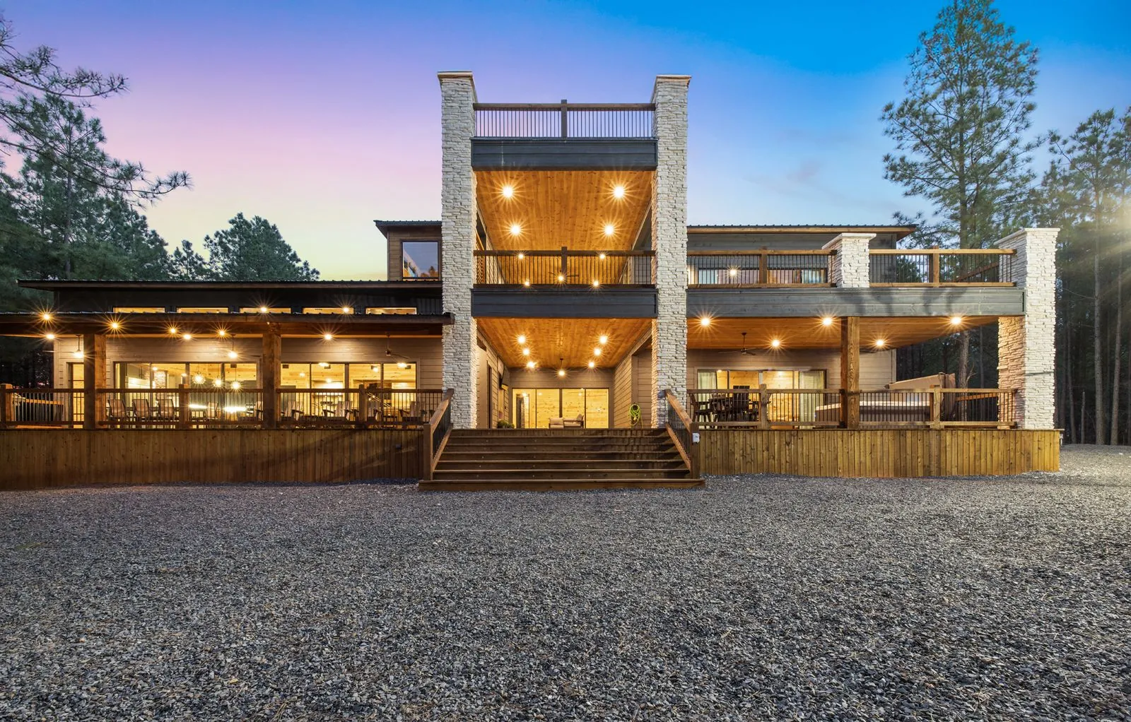 Front exterior of LivNLove at dusk with dual stone columns, multi-level decks, and warm interior glow