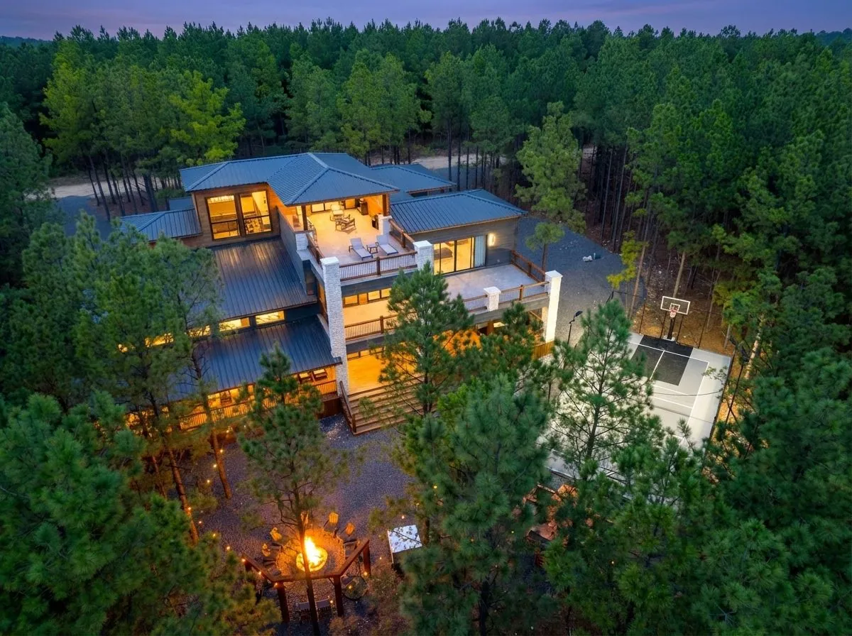 Aerial twilight view of LivNLove luxury cabin in Broken Bow showing illuminated decks, fire pit, and forested surroundings